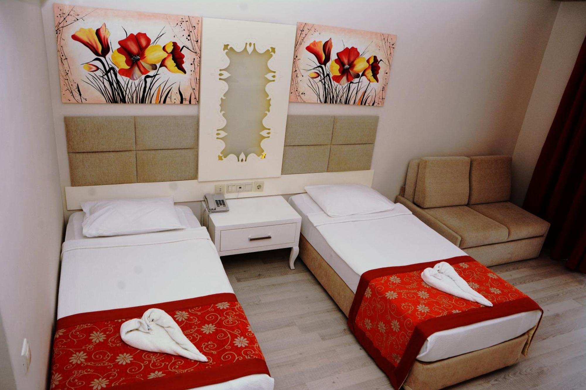 Miramor Hotel & Spa Antalya Exterior foto The photo shows a hotel room featuring two single beds with white linens, each adorned with a decorative red throw. The headboards are upholstered in a light beige fabric. Above the beds, there are two large artwork pieces depicting colorful flowers.